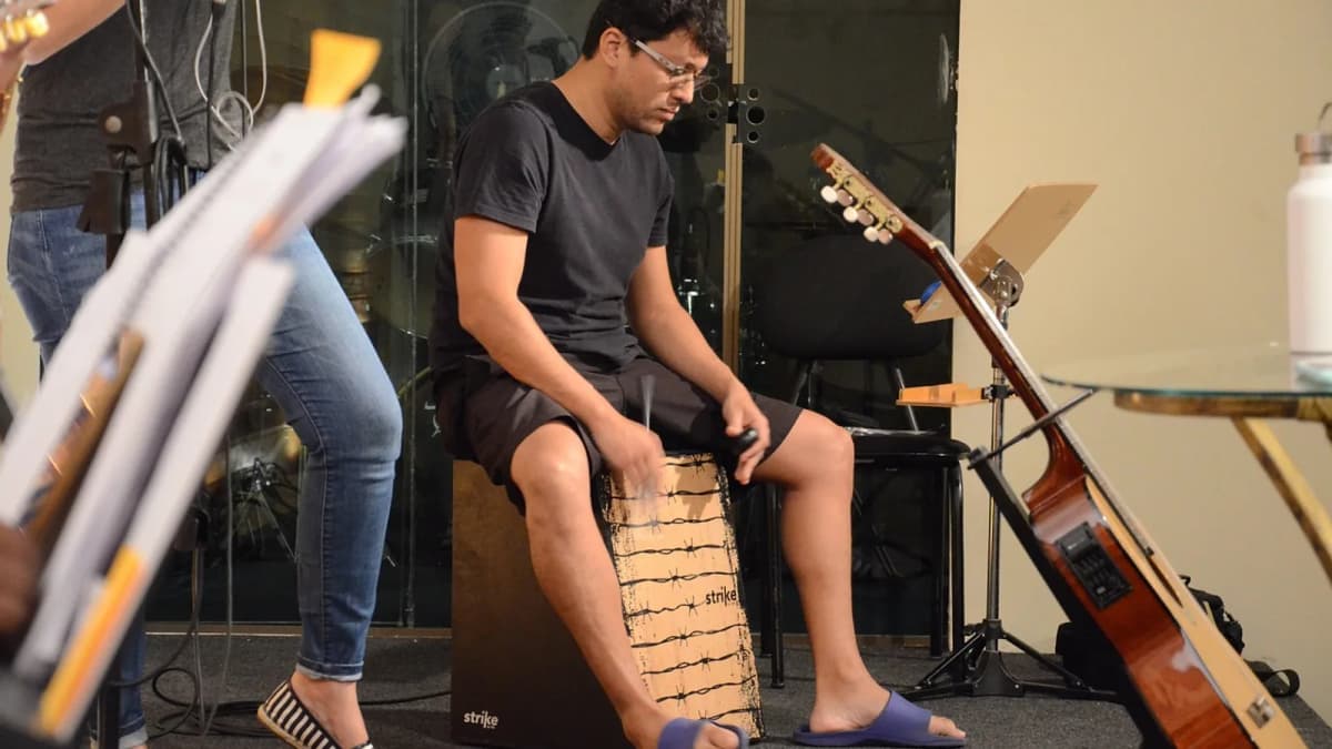 Ein Spieler sitzt auf einer Cajon und schlägt die Vorderplatte, dahinter Notenständer und eine Gitarre. Foto: u_veuaj3oo / Pixabay.