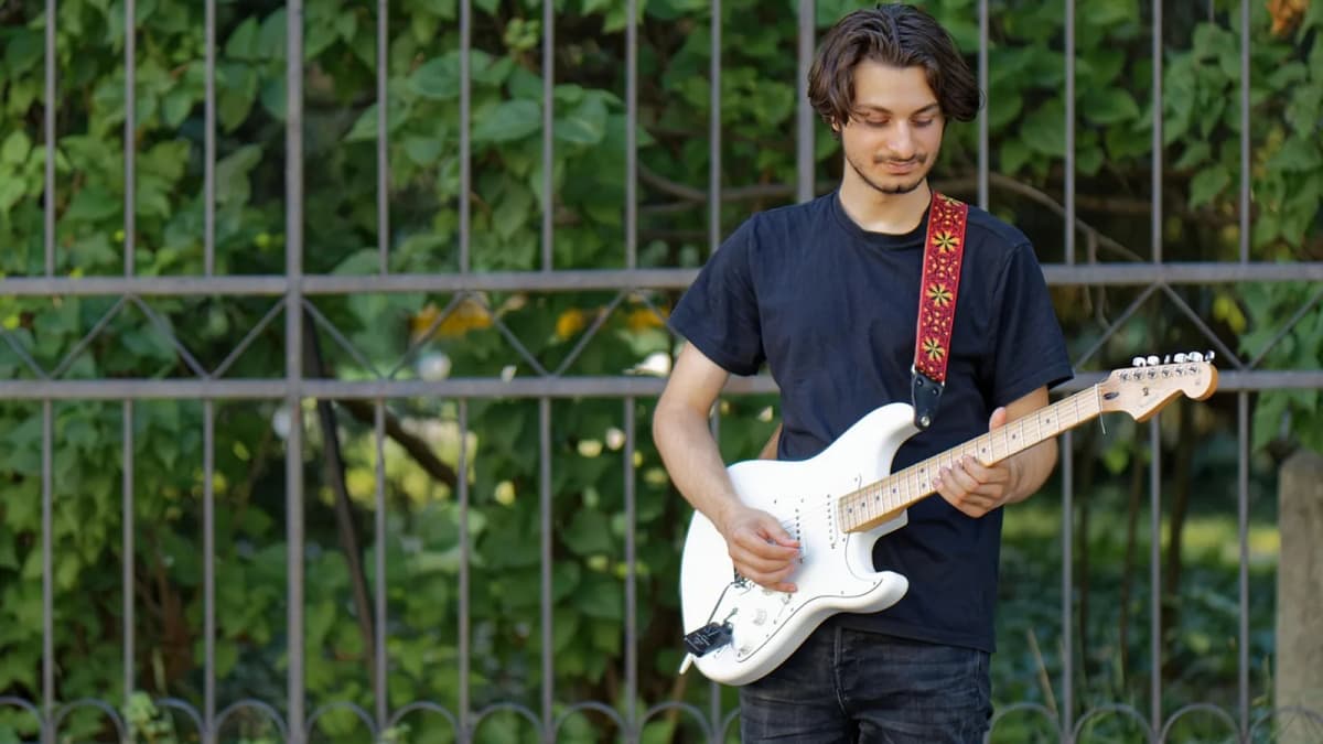 Ein junger Mann steht im Freien und spielt eine weiße E-Gitarre. Foto: Surprising_Media / Pixabay.