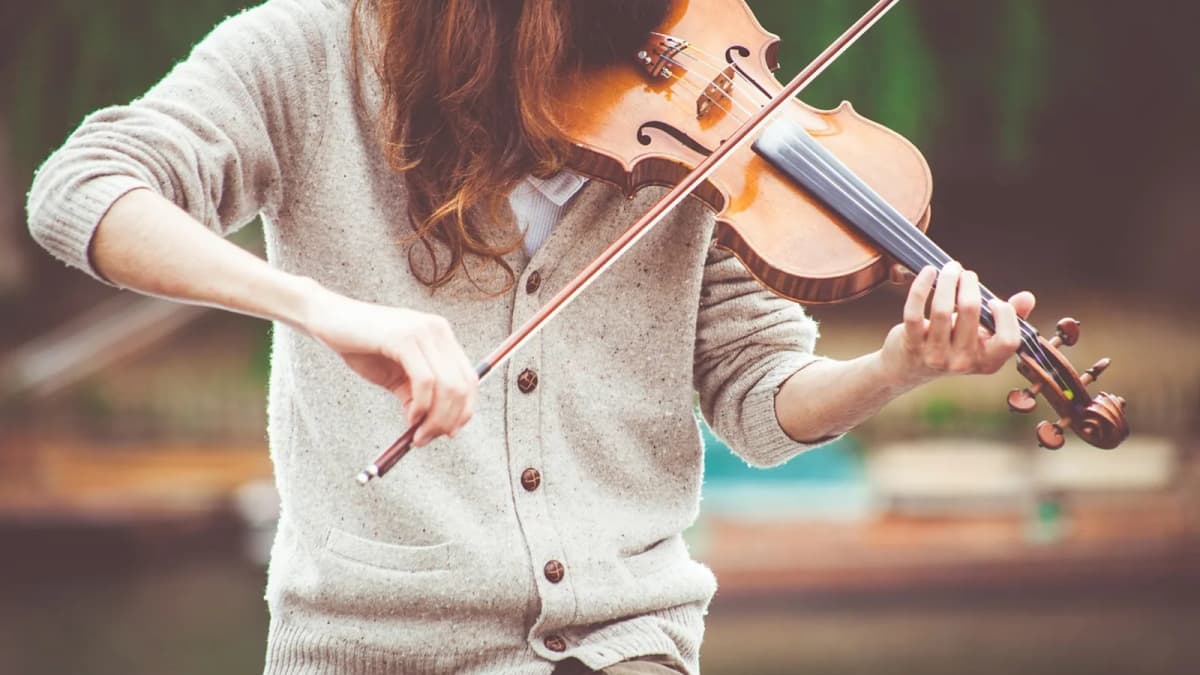Eine Frau in einem Pullover spielt Geige und führt den Bogen mit der rechten Hand. Foto: Pexels / Pixabay.