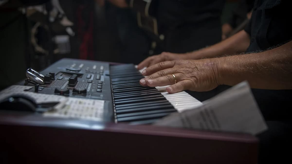 Hände spielen auf einem Bühnenkeyboard mit Reglerfeld, daneben liegt ein Notenblatt. Foto: 7144605 / Pixabay.