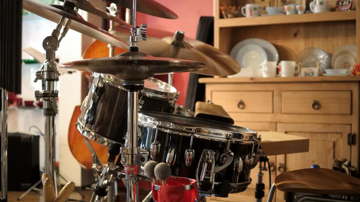 Ein Schlagzeug mit Becken und Snare steht in einem Wohnzimmer neben einem Regal mit Geschirr. Foto: Jirreaux / Pixabay.